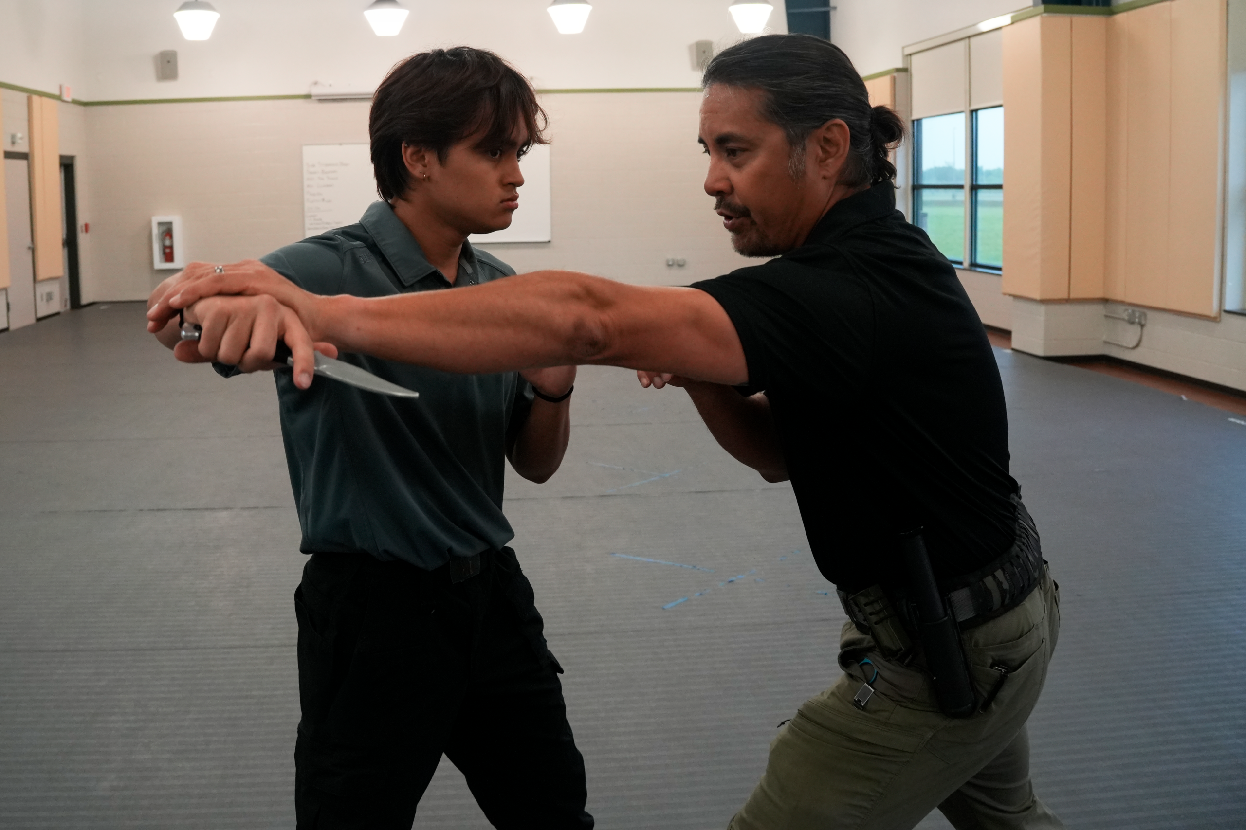 Two men fighting; the man on the left is holding a knife and the man on the right is trying to block him from striking with the knife