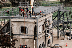Rescuers working on the top of a two story building using a wench to pull a car