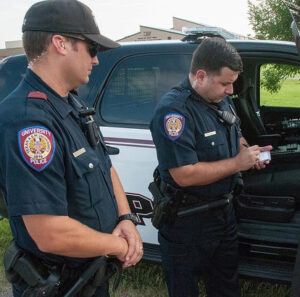 Male law enforcement supervising another male officer writing a ticket