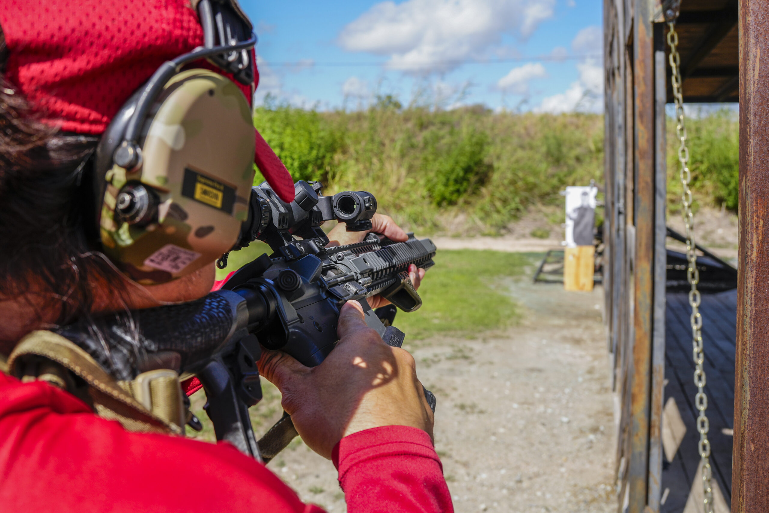  Man holding a magazine fed semi-automatic rifle in the shooting ready position while looking through an offset red dot sight optic.
