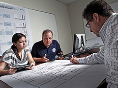 One female and two males sitting around a table working on a desktop plan