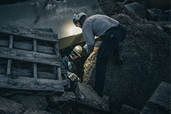Two rescuers going inside a small, dark opening in a pile of rubble