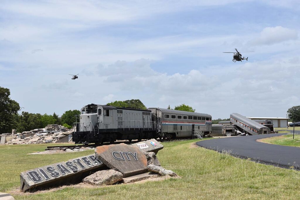 two helicopters flying over a train and Disaster City sign
