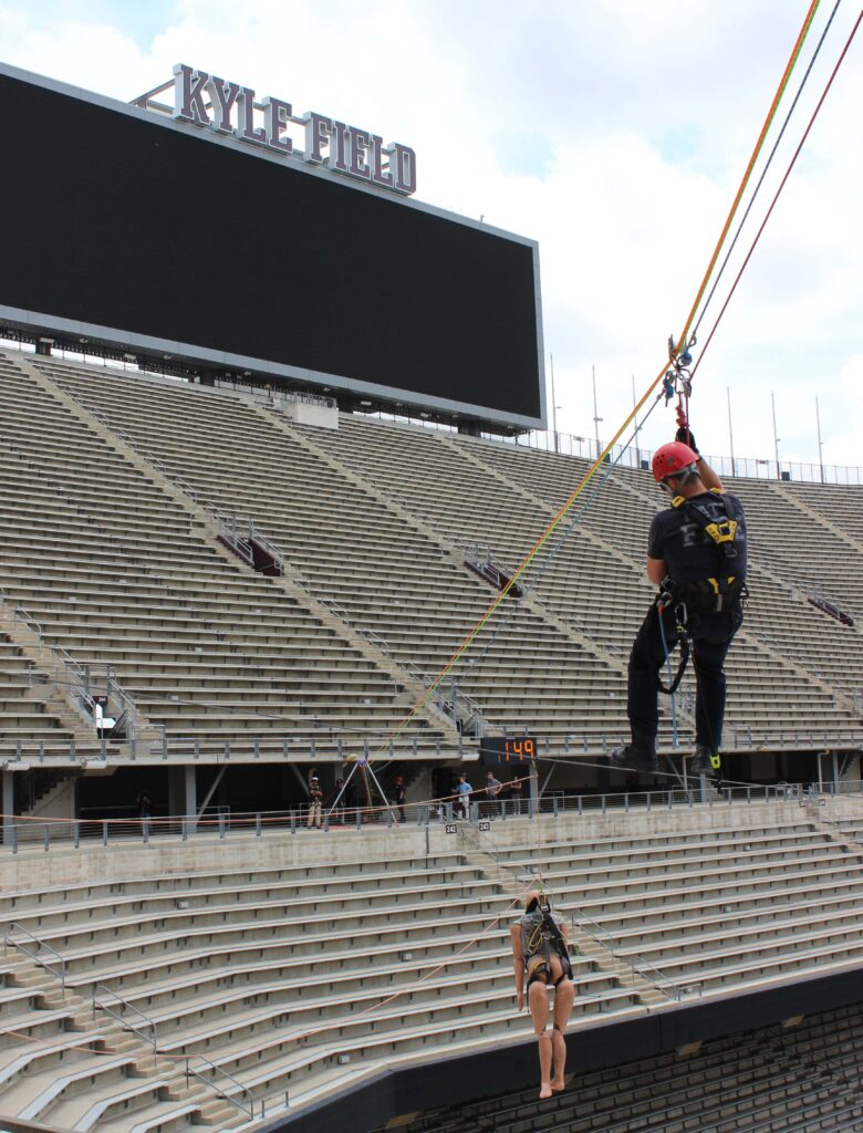man zip lining to save a person stuck in the air over a stadium
