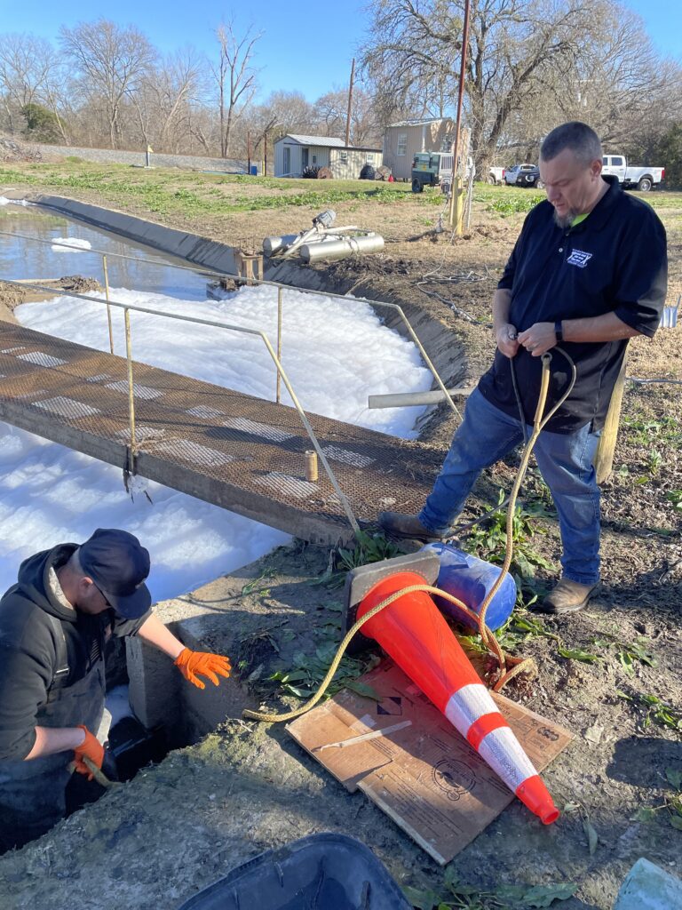 TEEX’s Jason Barber (right) assists Cumby water system staff member Tyler Humphries in plugging a wastewater main line and reinvigorating the microorganisms that treat wastewater.