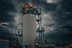 workers standing a top a very large verticle tank