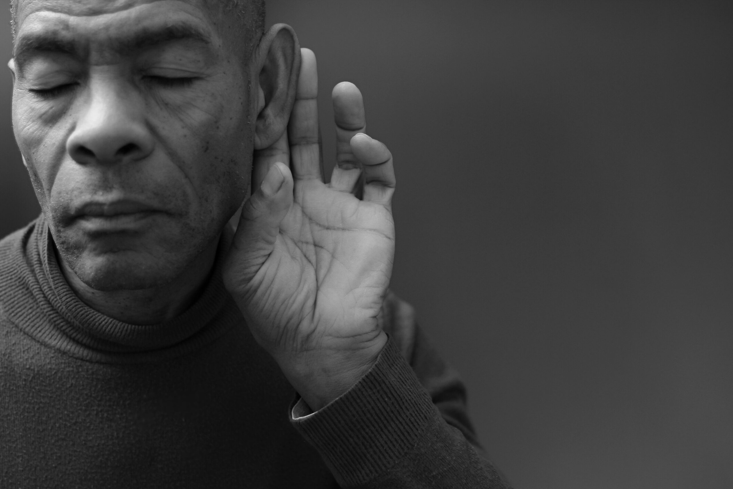 Man suffering from hearing loss holding his hand up by his ear to hear better